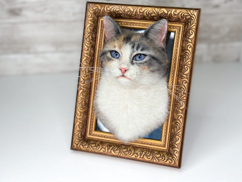 May include: A three-dimensional cat portrait sculpture featuring a calico cat with blue eyes, a pink nose, and white chest fur, mounted inside an ornate, rectangular, antique-style gold-toned frame with intricate embossed scrollwork patterns.