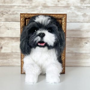 May include: A handcrafted needle felted sculpture of a black and white Shih Tzu dog with a fluffy coat, dark eyes, and a small black nose. The dog is positioned in front of an ornate, rectangular, antique-style gold picture frame.