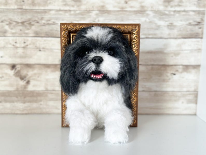 May include: A handcrafted needle felted sculpture of a black and white Shih Tzu dog with a fluffy coat, dark eyes, and a small black nose. The dog is positioned in front of an ornate, rectangular, antique-style gold picture frame.
