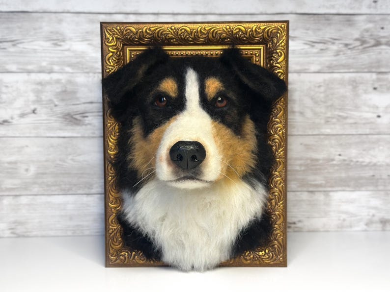May include: A needle-felted dog head sculpture featuring black, white, and tan fur, mounted within an ornate, rectangular gold-coloured frame. The dog has brown eyes, a black nose, and a white blaze extending from the forehead to the chest.