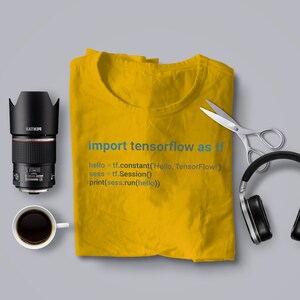 May include: A yellow t-shirt with the text "import tensorflow as tf" and a code snippet printed on it. The code snippet is "hello = tf.constant('Hello, TensorFlow!') sess = tf.Session() print(sess.run(hello))"