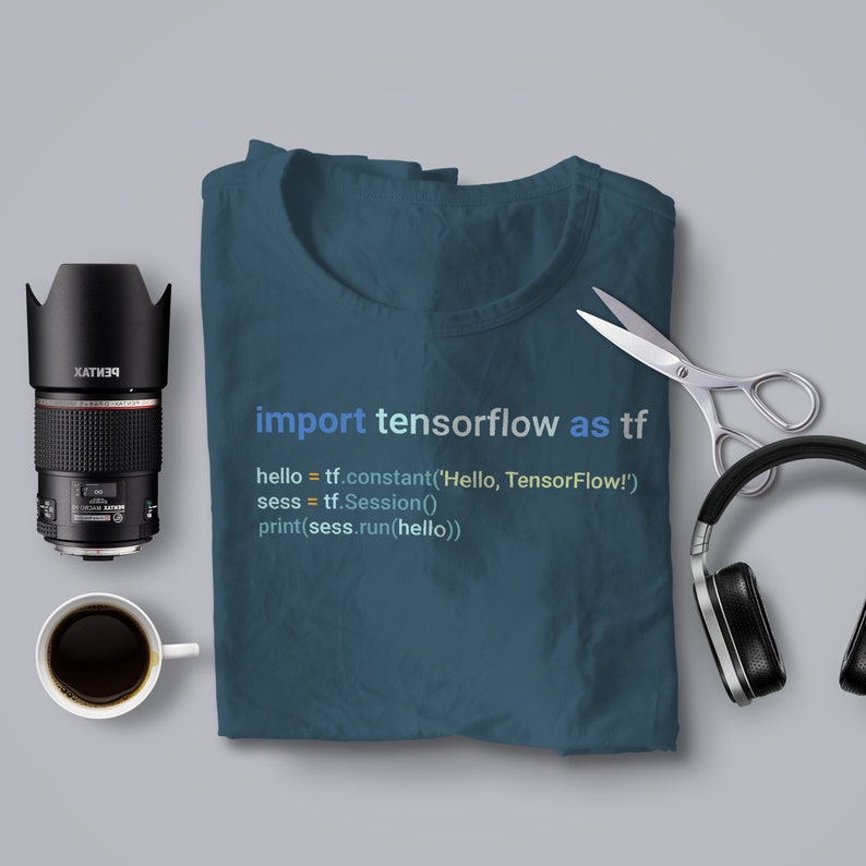 May include: A teal blue t-shirt with the code "import tensorflow as tf" printed on it. The code is written in a light blue font. The t-shirt is folded and laid flat on a grey surface.