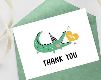 May include: A green alligator wearing a party hat holds a yellow heart with the name "Jayden" on it. The card says "Thank You".