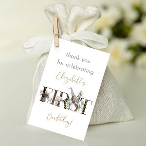 May include: White favor bag with a thank you tag that says "Thank you for celebrating Elizabeth's First Birthday!" The tag has a gold glitter design with animal illustrations.