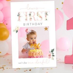Pu&ograve; includere: Un cartello di primo compleanno stampabile rosa e bianco con accenti floreali. Il cartello dice "Lexi's First Birthday" e ha una cornice per foto con una foto di una bambina che indossa una corona e tiene un dolce. Il testo sotto la cornice per foto dice "Isn't she one-derful!"