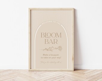 May include: A printable sign for a "Bloom Bar" with a light brown background and white and brown text. The sign features a stylized arch with a floral design and the text "Welcome to the Bloom Bar. Make a bouquet to take on your way! Thank you for celebrating with us!"