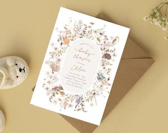 Op de afbeelding: Een witte rechthoekige uitnodigingskaart voor een babyshower met een centraal ovaal kader met de tekst "please join us for baby shower honoring Chloe" en evenementdetails, omringd door een botanische krans met illustraties van bosdieren.