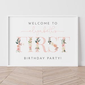 Pu&ograve; includere: Un cartello bianco con un design floreale rosa che dice "Benvenuti al primo compleanno di Elizabeth!"