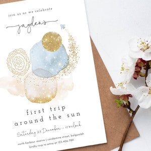 May include: A white invitation card with gold glitter accents and blue watercolor circles. The text reads "Join us as we celebrate Jayden's first trip around the sun. Saturday 29 December - 11 o'clock. North Harbour Reserve | Condamine Street, Balgowlah. Kindly RSVP to Anna at 123-456-789."
