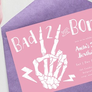 Puede incluir: Tarjeta de invitaci&oacute;n rosa con una mano de esqueleto blanca haciendo un signo de paz. El texto en la tarjeta dice "Bad 2 the Bone" y "Anita's 2nd Birthday!" con detalles para el evento.