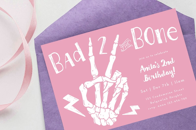 Puede incluir: Tarjeta de invitaci&oacute;n rosa con una mano de esqueleto blanca haciendo un signo de paz. El texto en la tarjeta dice "Bad 2 the Bone" y "Anita's 2nd Birthday!" con detalles para el evento.