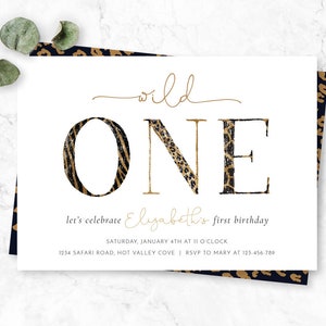 May include: A white invitation card with the words "wild ONE" in gold and animal print lettering. The text "let's celebrate Elizabeth's first birthday" is below. The card has a leopard print border and eucalyptus leaves.