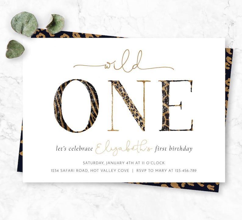 May include: A white invitation card with the words "wild ONE" in gold and animal print lettering. The text "let's celebrate Elizabeth's first birthday" is below. The card has a leopard print border and eucalyptus leaves.