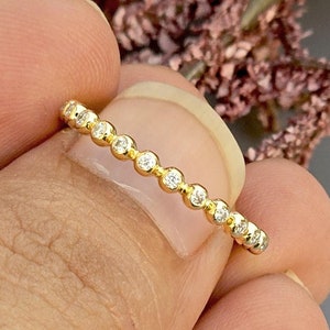 May include: A delicate gold band ring with a row of small, clear gemstones.