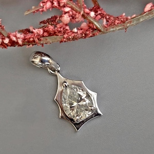 Puede incluir: Un colgante de plata con una piedra preciosa transparente en forma de pera engastada en un diseño de estrella.