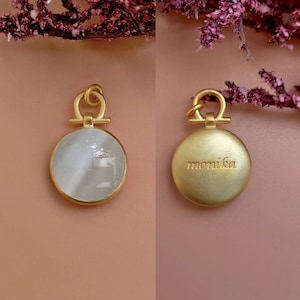 May include: A gold-toned pendant with a round, white, mother-of-pearl front and a gold back engraved with the word "monika".