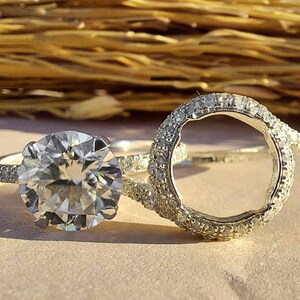 Pode incluir: Duas alianças de noivado de prata com um grande diamante transparente no centro de uma das alianças. A outra aliança é um engaste de halo com uma abertura redonda no centro.