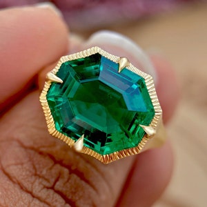 Peut inclure: Une bague en or avec une grande pierre précieuse de couleur vert émeraude de forme octogonale. La bague est sertie dans une bande d'or avec un bord texturé.