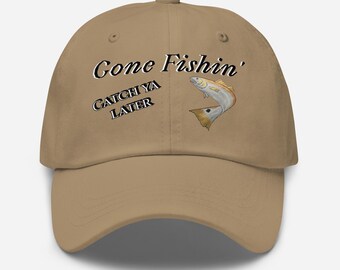 Puede incluir: Gorra de béisbol beige con el texto "Gone Fishin'" en blanco y negro, y "Catch Ya Later" en blanco y negro. Una ilustración de un pez de dibujos animados está en el lado derecho de la gorra.