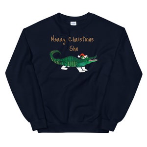 May include: Navy blue sweatshirt with a green alligator wearing a Santa hat. The text "Merry Christmas Sha" is printed on the sweatshirt.