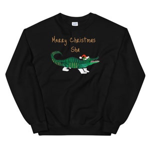 May include: Black Christmas sweatshirt with a green alligator wearing a Santa hat and the text "Merry Christmas Sha" in gold.