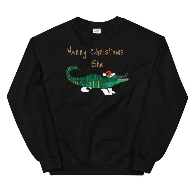 May include: Black Christmas sweatshirt with a green alligator wearing a Santa hat and the text "Merry Christmas Sha" in gold.