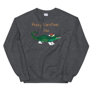 May include: A dark gray sweatshirt with a green alligator wearing a red Santa hat. The text "Merry Christmas Sha" is printed in orange on the front of the sweatshirt.