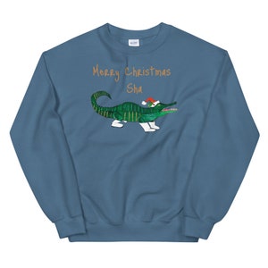 May include: A blue sweatshirt with the text "Merry Christmas Sha" in orange. A green alligator wearing a red Santa hat is printed on the sweatshirt.