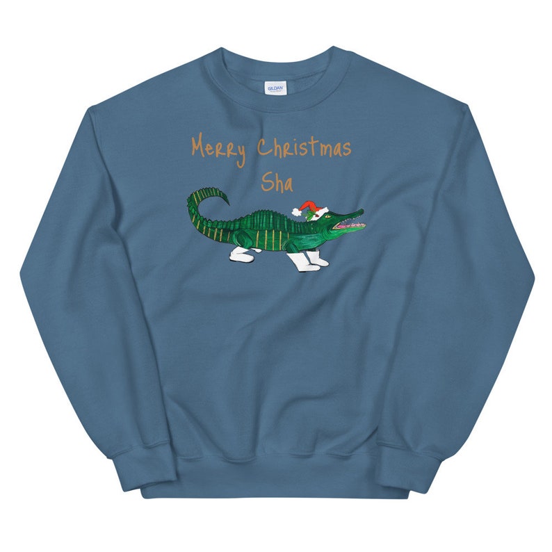 May include: A blue sweatshirt with the text "Merry Christmas Sha" in orange. A green alligator wearing a red Santa hat is printed on the sweatshirt.