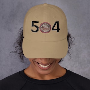 May include: A tan baseball cap with the number "504" in black block letters. A circular graphic with the words "WATER METER" is between the numbers. The cap is worn by a person.