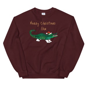 May include: Burgundy sweatshirt with a green alligator wearing a Santa hat. The text "Merry Christmas Sha" is printed in gold on the front.