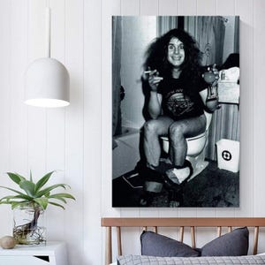 May include: Black and white print of a person sitting on a toilet, holding a cigarette and a drink. The person is wearing a t-shirt with a graphic design. The background includes a shower curtain and a trash can.