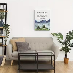 May include: A canvas print with a watercolour landscape of mountains and trees in blue and green hues. The print displays the text "WHEN MY HEART IS OVERWHELMED; LEAD ME TO THE ROCK THAT IS HIGHER THAN I Psalm 612."