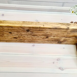 May include: A rustic wooden shelf with a natural wood finish and angled brackets. The shelf is mounted on a white wall.