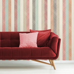 Puede incluir: Un sof&aacute; de terciopelo rojo con patas de madera delante de una pared con un patr&oacute;n de rayas de chevron naranja, rosa, azul y marr&oacute;n.