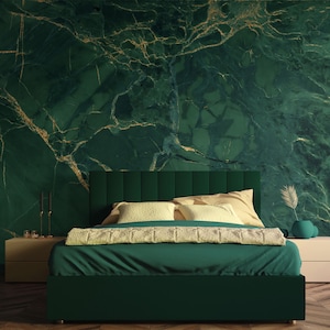 May include: A green velvet bed with a white and beige patterned throw blanket and two pillows. The bed is in front of a green marble wall with gold veins.
