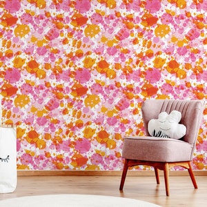 May include: A pink and orange splatter paint pattern wallpaper with a pink chair and a white rug in front of it.