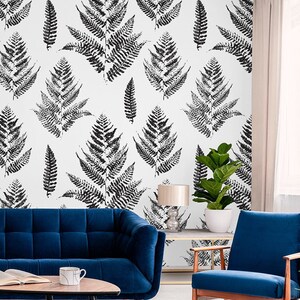 K&ouml;nnte beinhalten: Ein Wohnzimmer-Interieur mit einem blauen Samtsofa, zwei blauen Sesseln, einem goldenen Metallstuhl, einem Couchtisch, einer Topfpflanze und einem kleinen Hund. Die Wand ist mit einer schwarz-wei&szlig;en Farnmuster-Tapete dekoriert.