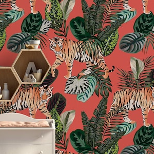 Könnte beinhalten: Eine korallenfarbene Tapete mit einem sich wiederholenden Muster aus Tigern und tropischen Blättern. Die Tapete ist in einem Kinderzimmer mit einem Kinderbett und einer Wickelkommode zu sehen.