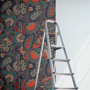 May include: A silver step ladder is positioned in front of a wall covered in teal and orange floral wallpaper. Two rolls of wallpaper are on the floor.