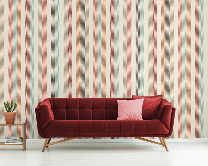 Puede incluir: Un sof&aacute; de terciopelo rojo con patas de madera delante de una pared con un patr&oacute;n de rayas de chevron naranja, rosa, azul y marr&oacute;n.