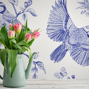May include: A blue and white floral wallpaper with a bluebird design. A bouquet of pink tulips is in a light blue pitcher in the foreground.