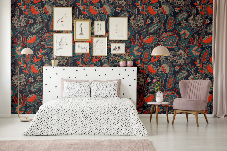 May include: A bedroom with a white bed with black polka dots bedding and a pink armchair. The wall is covered in a dark blue wallpaper with a floral pattern in orange, teal, and brown. There are framed pictures on the wall.