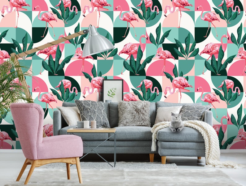 May include: A pink and green geometric wallpaper featuring pink flamingos and tropical leaves. The wallpaper is in a living room setting with a pink armchair, a gray sofa, and a gray cat.