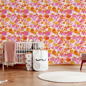May include: A nursery room with a white crib, a rocking horse, a pink armchair, and a white rug. The walls are covered in a pink and orange splatter paint wallpaper.
