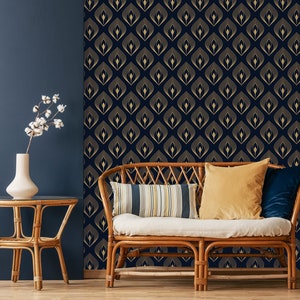 Pode incluir: Um sof&aacute; de vime com almofadas brancas e almofadas decorativas fica em frente a uma parede azul escura com papel de parede geom&eacute;trico dourado.