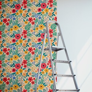 May include: A roll of floral wallpaper with a colorful pattern of red, yellow, blue, and green flowers on a cream background. A silver step ladder is next to the wallpaper roll.