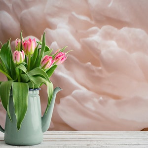 K&ouml;nnte beinhalten: Ein Strau&szlig; rosa und wei&szlig;er Tulpen in einem hellblauen Emaille-Krug auf einem wei&szlig;en Holztisch. Der Hintergrund ist ein weiches, pfirsichfarbenes abstraktes Design.