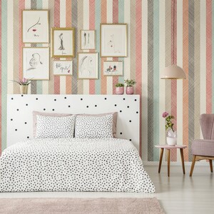 Puede incluir: Un dormitorio con una cama blanca con lunares negros, un sill&oacute;n rosa y una mesita de noche con un jarr&oacute;n de flores. Las paredes est&aacute;n cubiertas con un papel tapiz estampado con rayas verticales de color rojo, naranja, verde y marr&oacute;n.