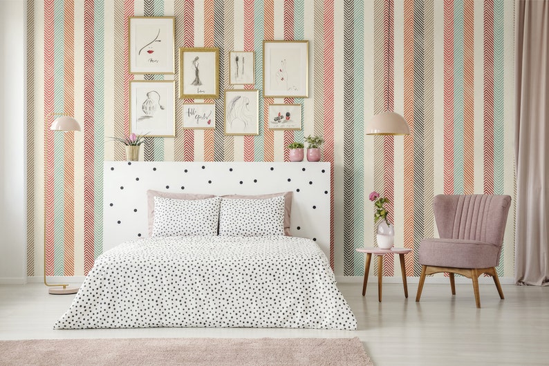 Puede incluir: Un dormitorio con una cama blanca con lunares negros, un sill&oacute;n rosa y una mesita de noche con un jarr&oacute;n de flores. Las paredes est&aacute;n cubiertas con un papel tapiz estampado con rayas verticales de color rojo, naranja, verde y marr&oacute;n.
